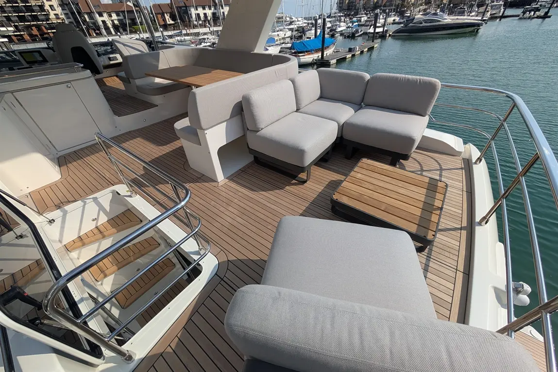 Stylish yacht deck with grey lounge furniture, wooden table, and marina view, featuring blue boats and water.